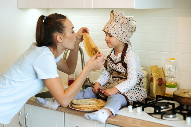 Mignonne petite fille à la maison avec sa belle mère fait des crêpes dans une cuisine blanche