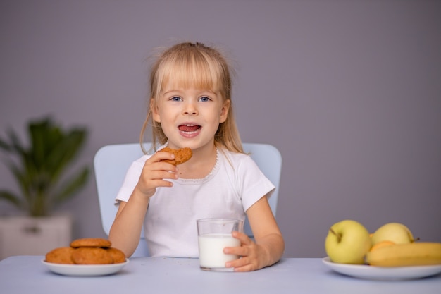 Mignonne petite fille mangeant des biscuits et buvant du lait à la maison ou à la maternelle