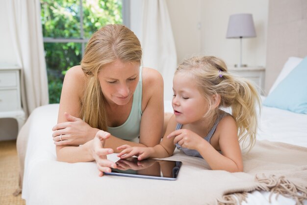 Mignonne petite fille et mère sur le lit avec tablette