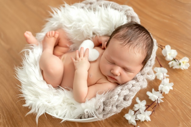 Mignonne petite fille nouveau-née de 0 à 14 jours dormant dans un berceau avec des fleurs. Modèle pour l'emballage des produits pour enfants. Portrait en gros plan d'un nouveau-né avec un sourire sur son visage.