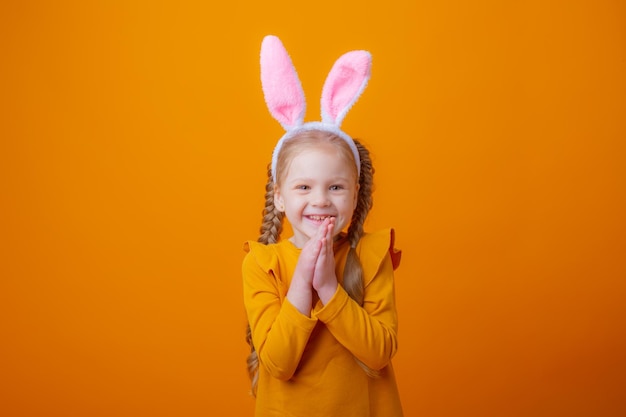 Mignonne petite fille avec des oreilles de lapin de Pâques sur un fond jaune montre différentes émotions joie de rêver