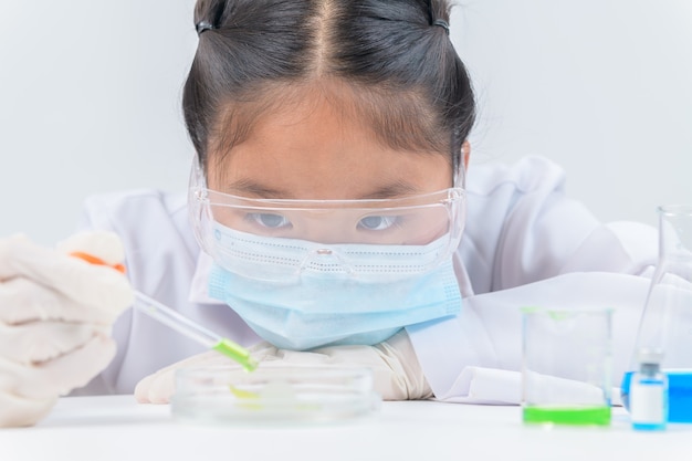 Mignonne petite fille portant des lunettes de sécurité et une blouse de laboratoire faisant l'expérience et en utilisant le compte-gouttes en laboratoire de chimie, l'éducation et le concept scientifique