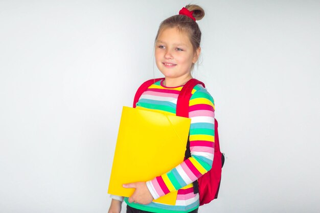 Mignonne petite fille portant un sac à dos rouge debout sur fond blanc, place pour le texte, retour au concept de l'école