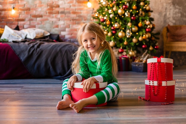Mignonne petite fille en pyjama près de l'arbre de Noël sort de la boîte-cadeau chaton
