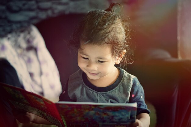 Photo une mignonne petite fille qui lit un livre à la maison.