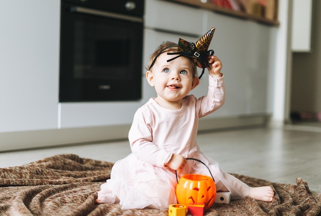 Mignonne petite fille en robe rose avec le chapeau de la sorcière et la lanterne de citrouille assise sur le sol dans la cuisine à l'heure d'Halloween à la maison
