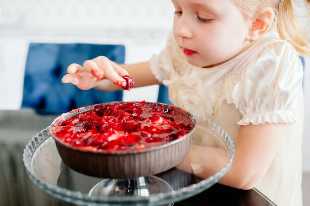 Mignonne petite fille rousse manger un gâteau avec ses mains dans une belle cuisine lumineuse pour son anniversaire