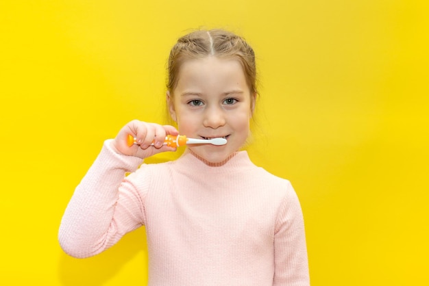 Mignonne petite fille se brosser les dents sur fond jaune