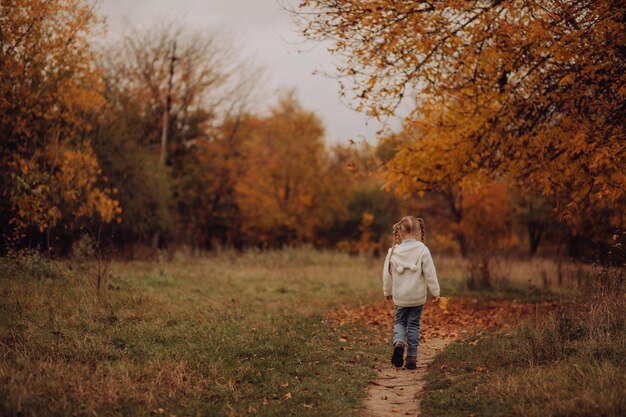 Photo mignonne petite fille se promène dans le parc en automne enfant joue derrière l'arbre avec des feuilles jaunes orange sourit jeux famille loisirs aventure voyage amusant avec enfants concept de voyage et de vacances en famille heureux