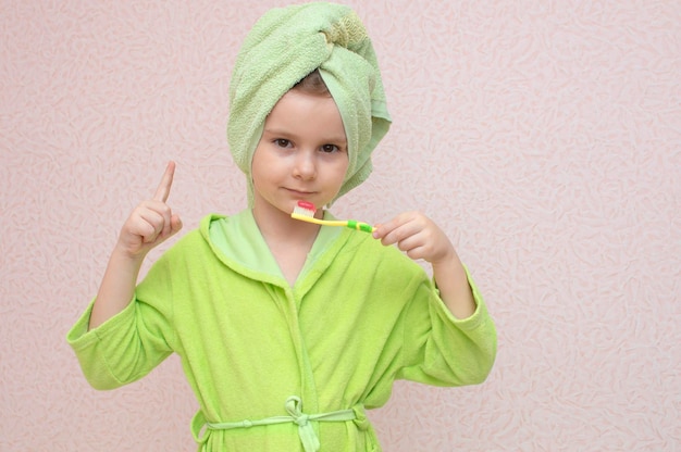 Mignonne petite fille avec une serviette sur la tête et un peignoir se brosse les dents. Dents saines. Enfance, hygiène bucco-dentaire, concept de procédures matinales.