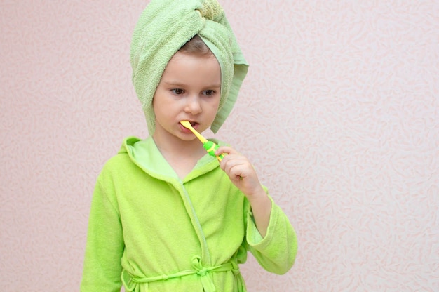 Mignonne petite fille avec une serviette sur la tête et un peignoir se brosse les dents. Dents saines. Enfance, hygiène bucco-dentaire, concept de procédures matinales.