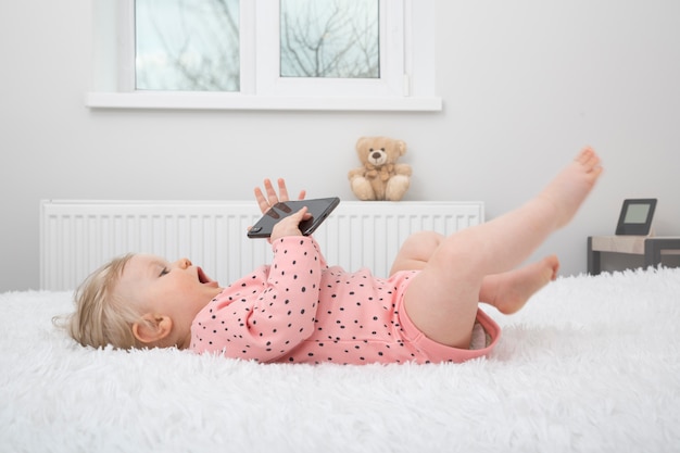 Mignonne petite fille avec un smartphone dans la chambre des parents.