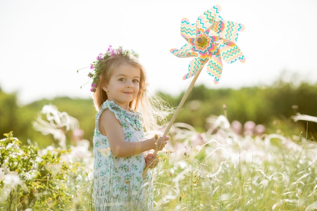 Mignonne petite fille souriant l'été sur le terrain tenant un moulin à vent