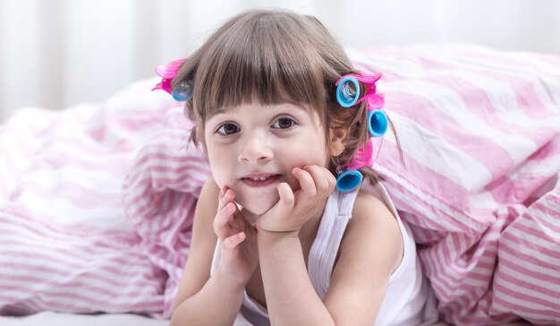 Mignonne petite fille souriante en position couchée dans un lit blanc confortable