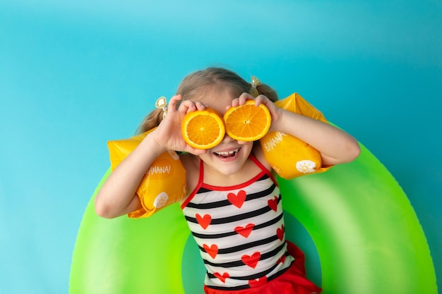 Mignonne petite fille sourit et tient des tranches d'orange devant ses yeux Fond bleu isolé