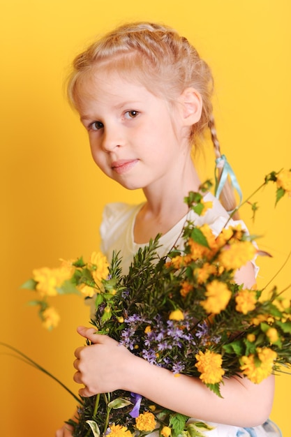 Mignonne petite fille tenant des fleurs jaunes regardant la caméra Enfance