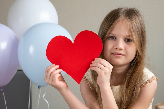 Mignonne petite fille tenant un grand coeur rouge et souriant félicitant maman pour la fête des mères