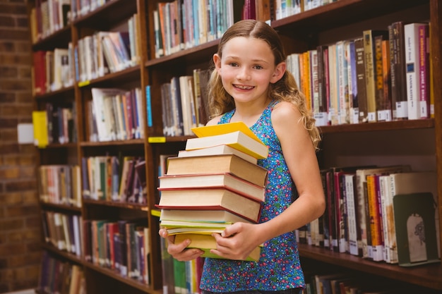 Mignonne petite fille transportant des livres dans la bibliothèque