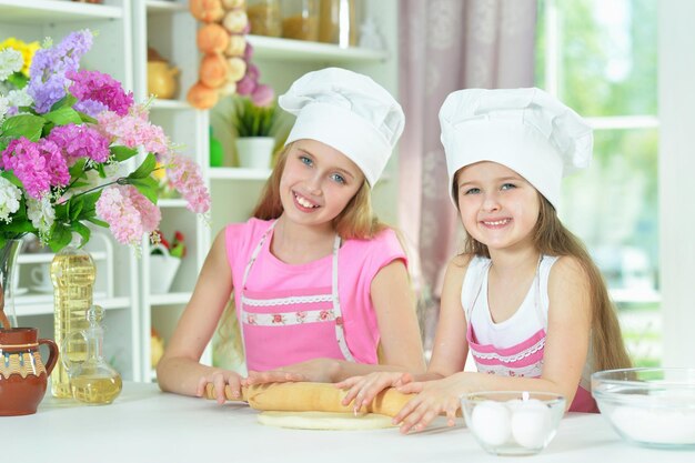 Mignonnes petites filles en chapeaux de chefs faisant de la pâte