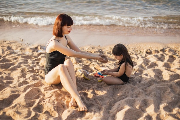 Mignonnes petites filles jouant avec du sable sur la plage et maman regardant doucement sa fille