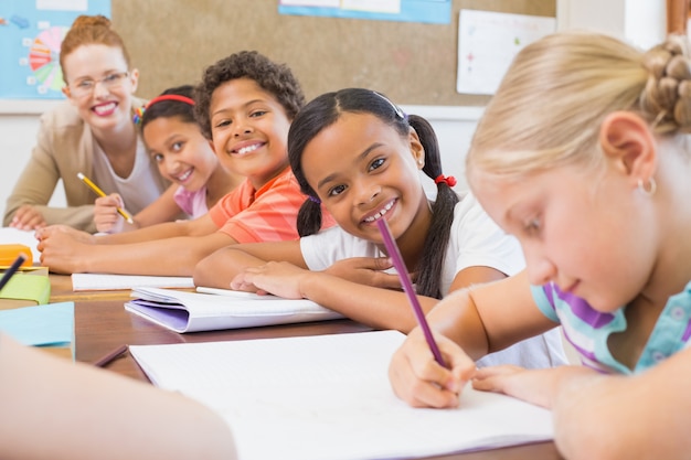 Mignons élèves écrivant au bureau dans la salle de classe