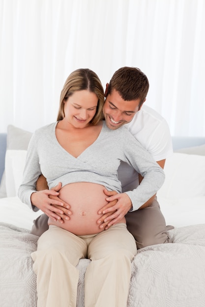 Mignons futurs parents en regardant le ventre de la femme assise sur le lit