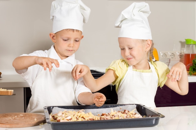 Mignons petits chefs d'enfant mettant des ingrédients sur la pizza sur le tableau blanc.