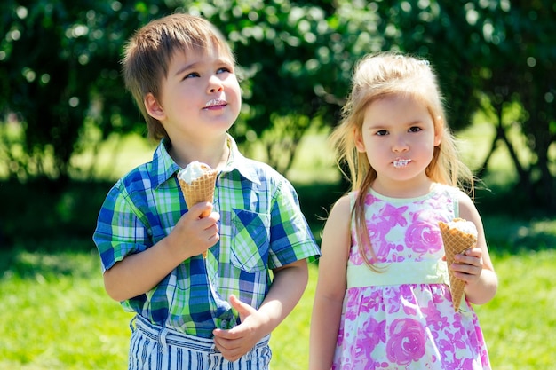 Mignons petits enfants garçon et fille mangent de la crème glacée aux taches dans une corne de gaufre enduite de visage dans le parc d'été