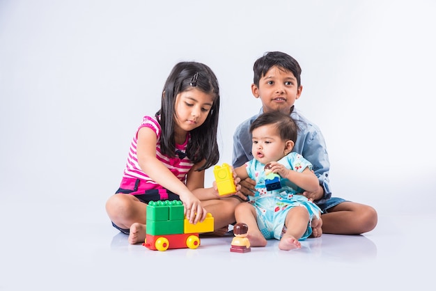 Mignons petits enfants indiens ou asiatiques jouant avec des jouets ou des blocs et s'amusant assis à table ou isolés sur fond blanc