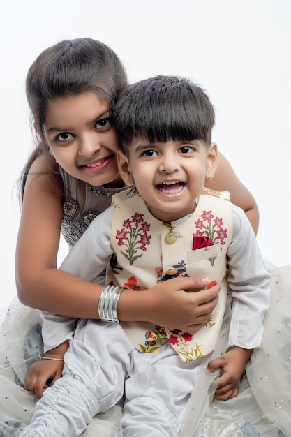 Mignons petits frères et sœurs asiatiques indiens debout et s'embrassant dans des vêtements blancs ethniques debout sur fond blanc