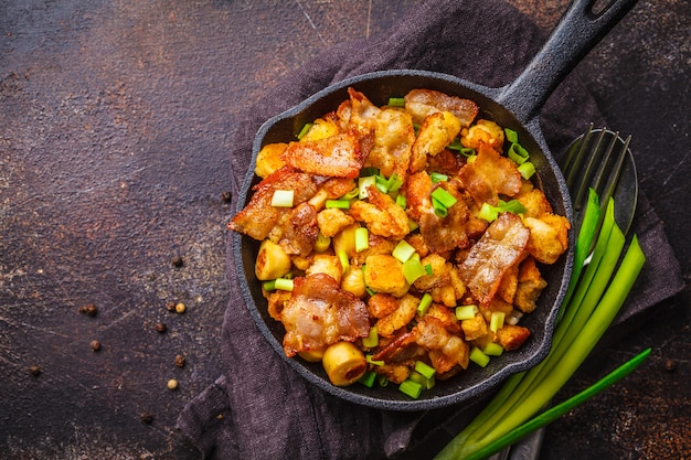 Migras espagnoles avec oignons verts et porc dans une poêle en fonte sur fond sombre.