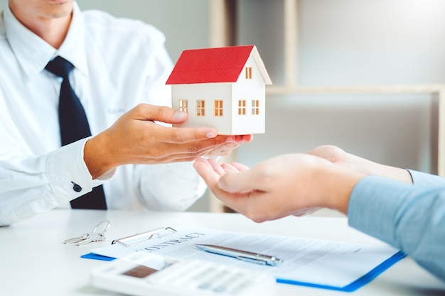 Le milieu de l'agent d'assurance donnant une maison modèle au client sur la table