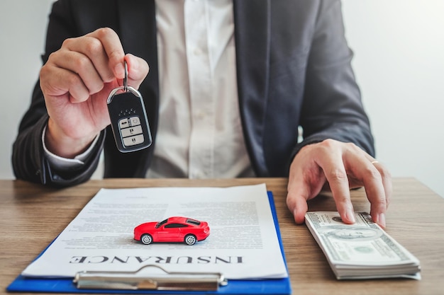 Le milieu d'un agent d'assurance tenant des clés de voiture et de la monnaie américaine.