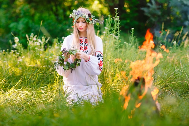 Milieu de l'été. Femme tissant une couronne près du feu.