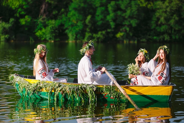 Milieu de l'été. Un groupe de jeunes en costumes nationaux navigue dans un bateau orné de feuilles et de phanères. Fête slave d'Ivan Kupala.