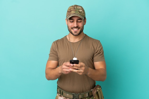 Militaire avec dog tag sur isolé sur fond bleu envoyant un message avec le mobile