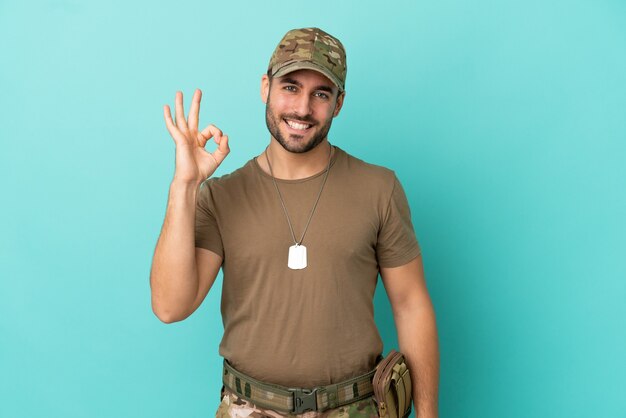 Militaire avec dog tag sur isolé sur fond bleu montrant signe ok avec les doigts