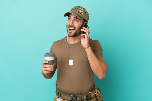 Militaire avec dog tag sur isolé sur fond bleu tenant du café à emporter et un mobile