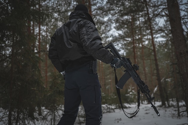 Photo un militaire privé avec un fusil ak-12 dans la forêt en hiver vue de l'arrière