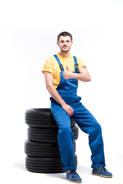 Militaire en uniforme bleu assis sur des pneus, fond blanc, réparateur avec pneus