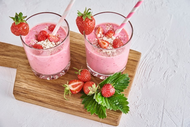 Milk-shake aux fraises en verre avec de la paille et des baies fraîches sur fond blanc
