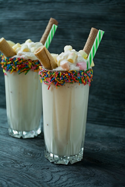 Milkshake à la banane avec crème glacée et crème fouettée, guimauves, biscuits, gaufres, servis dans une tasse en verre.