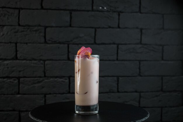 Milkshake blanc sucré original avec du jus de fraise avec des glaçons toniques et de la vodka sur une table noire dans le bar. Boissons alcoolisées