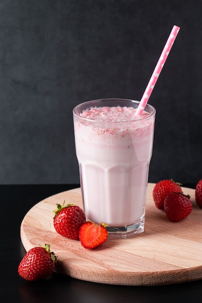 Milkshake frais aux fraises sur fond noir. Boisson d'été avec une paille dans un verre. Place pour le texte.