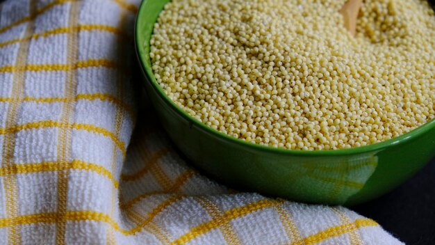 Millet dans un bol vert avec une cuillère en bois à l'intérieur, sur un torchon.