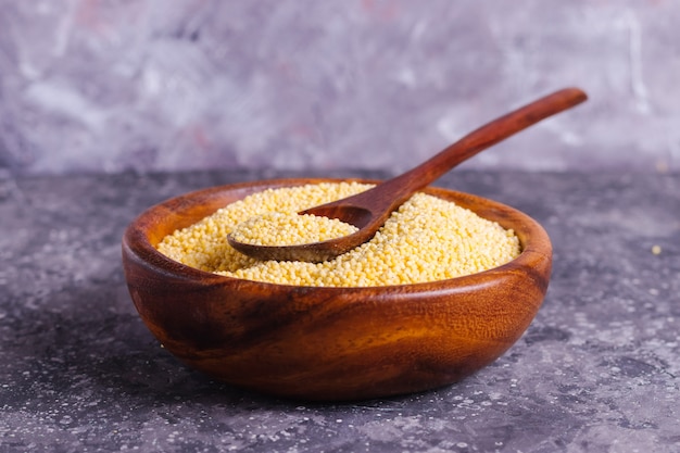 Millet jaune cru pour une bonne nutrition et santé dans une assiette en bois sur fond gris