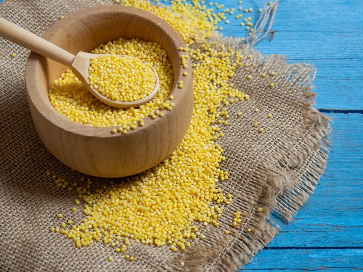 Photo millet. millet dans une cuillère et un bol en bois sur une table de cuisine en bois