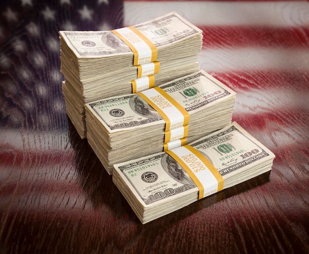 Des milliers de dollars empilés avec reflet du drapeau américain sur une table en bois
