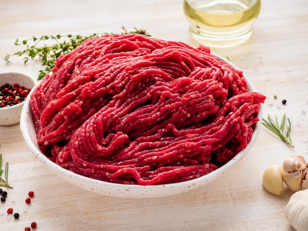 Mince boeuf, viande hachée avec des ingrédients pour la cuisson sur une table rustique en bois blanche