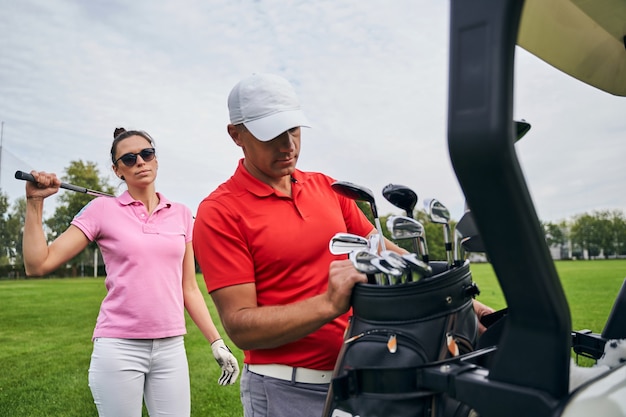 Mince golfeuse caucasienne aux cheveux noirs dans des lunettes de soleil debout derrière son entraîneur personnel dans une casquette